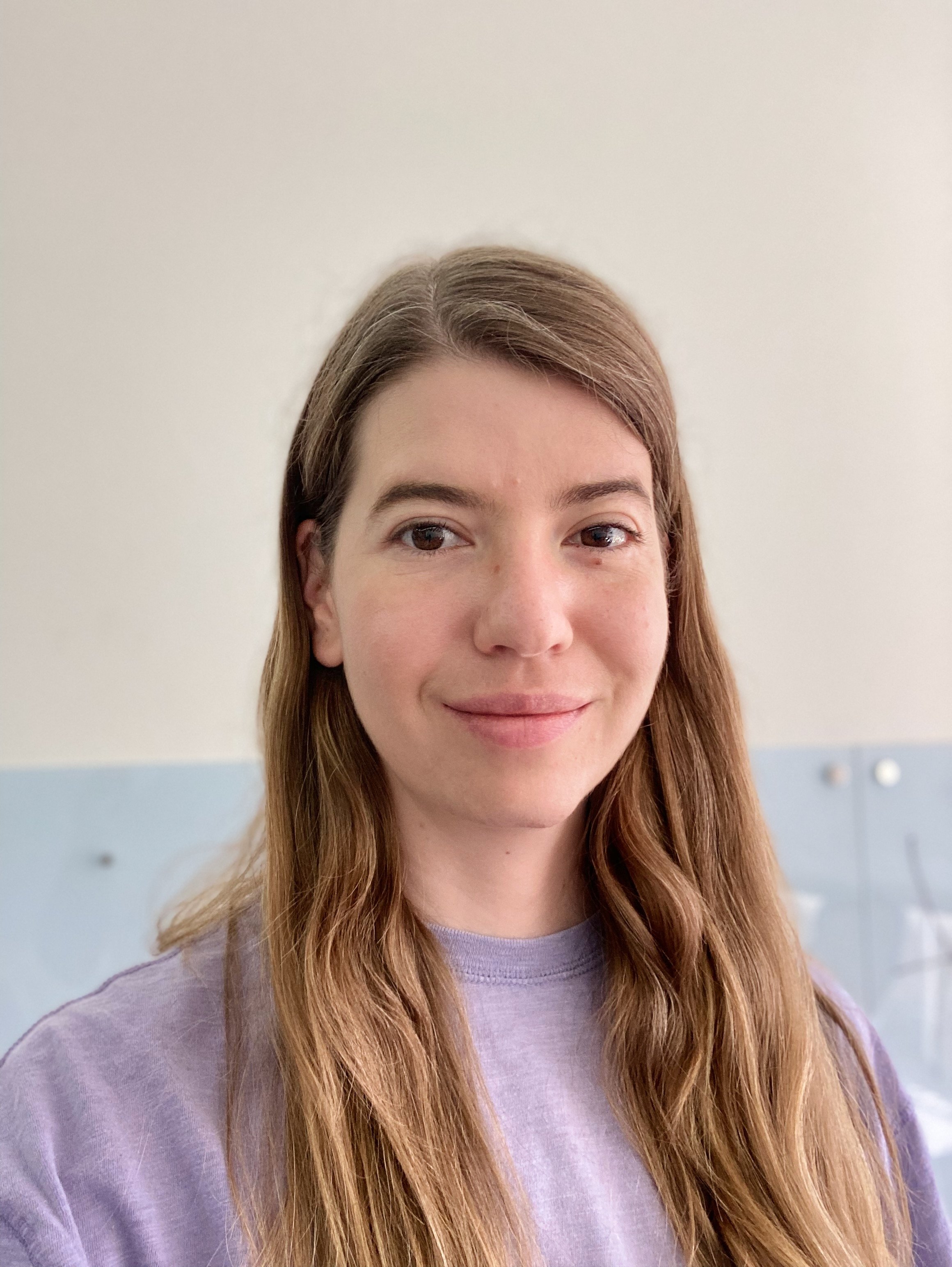 Woman with long light brown hair, wearing a lilac t-shirt, smiling at the camera.