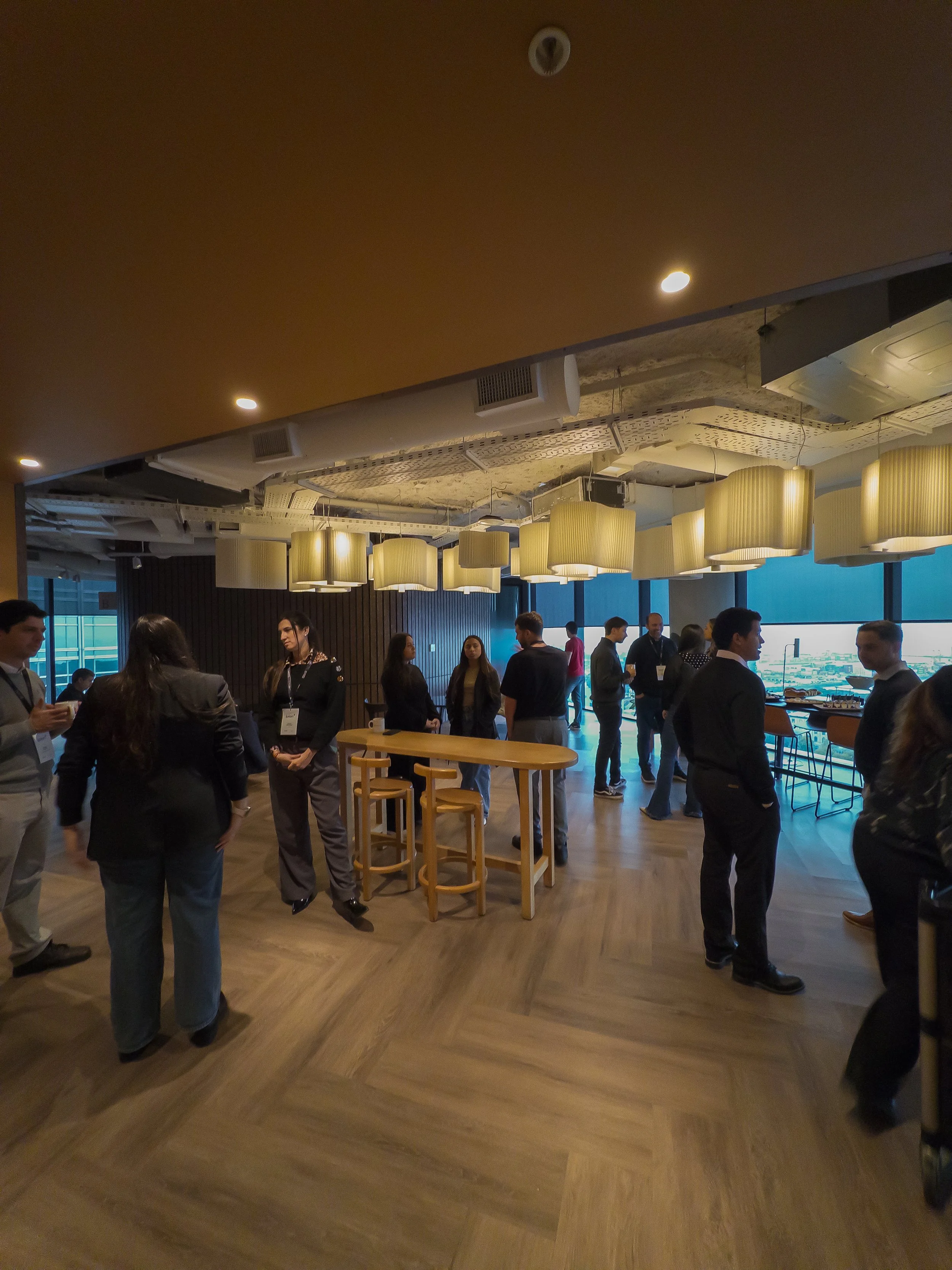 Grupo de personas en una sala moderna con techos bajos y lámparas decorativas, conversando en un evento o conferencia.