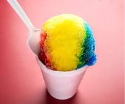A cup of rainbow-colored shaved ice with a spoon and straw against a pink background.