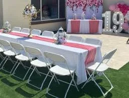 Outdoor 19th birthday party setup with a long table, white folding chairs, pink and white decorations, balloons, and floral arrangements.
