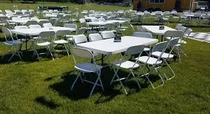 Several white tables and chairs arranged outdoors on a grassy area, possibly set up for an event or gathering.