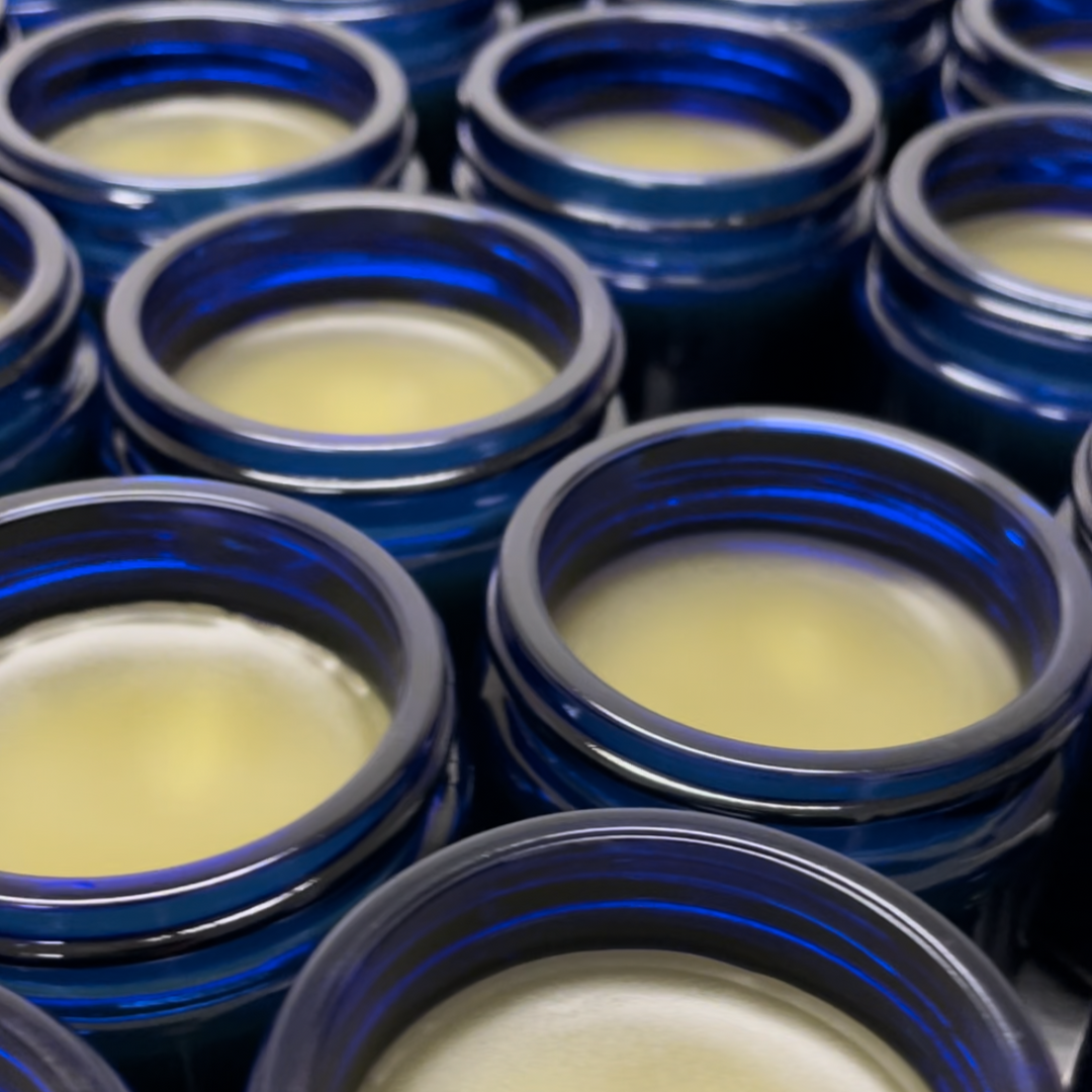 Multiple open dark blue glass jars filled with a light yellow, creamy substance, possibly candle wax.