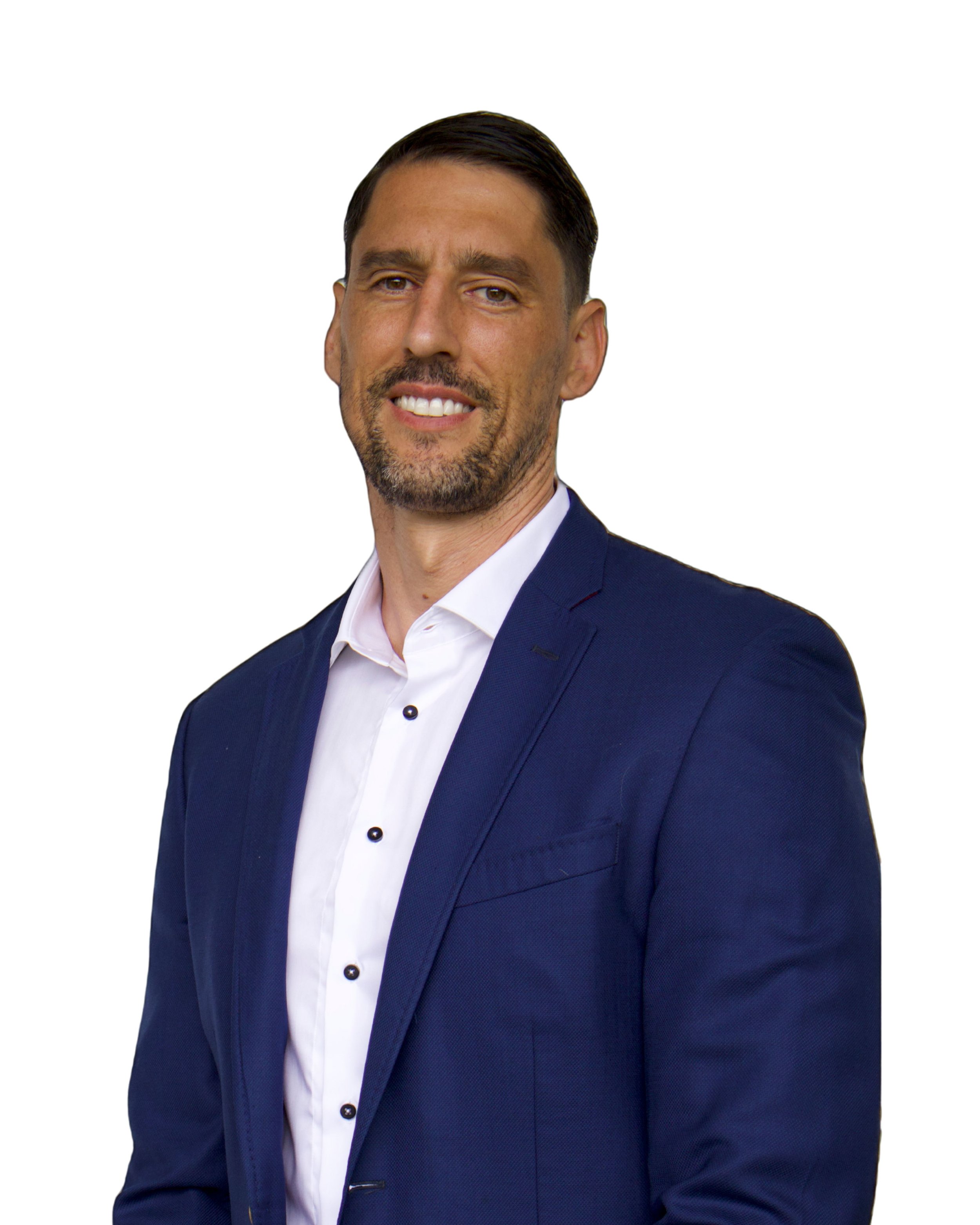 Portrait of a man with dark hair, styled back, wearing a navy blue suit and white shirt, smiling slightly, against a plain white background.