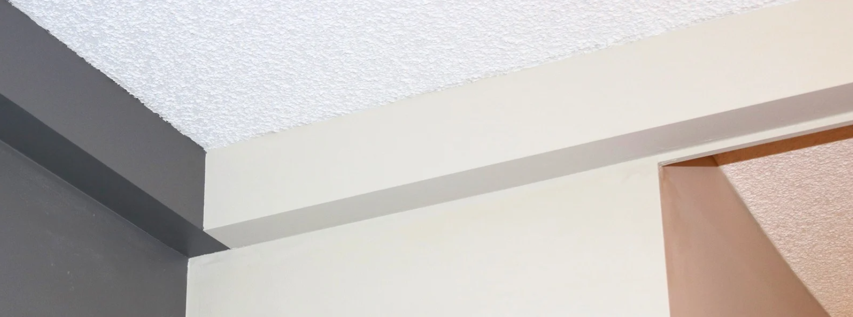 plumbing track installed and painted Close-up of ceiling corners with white, gray, and peach-colored walls and textured ceiling.