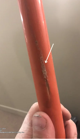 Close-up of a person's hand holding a piece of Kitec pipe showing failure