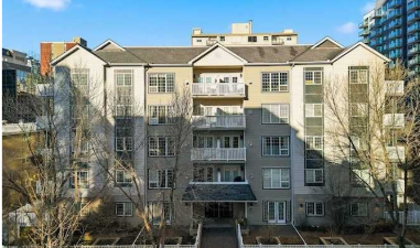A multi-story residential apartment building with a central entrance, balconies, and surrounded by leafless trees.