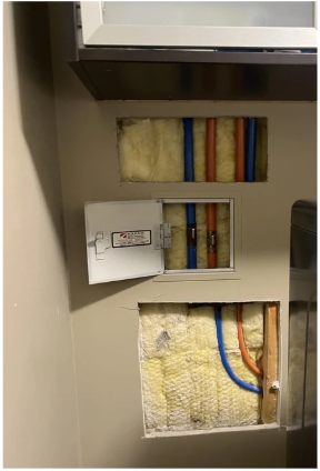 Open wall access panel showing electrical wiring and insulation and Kitec pipe