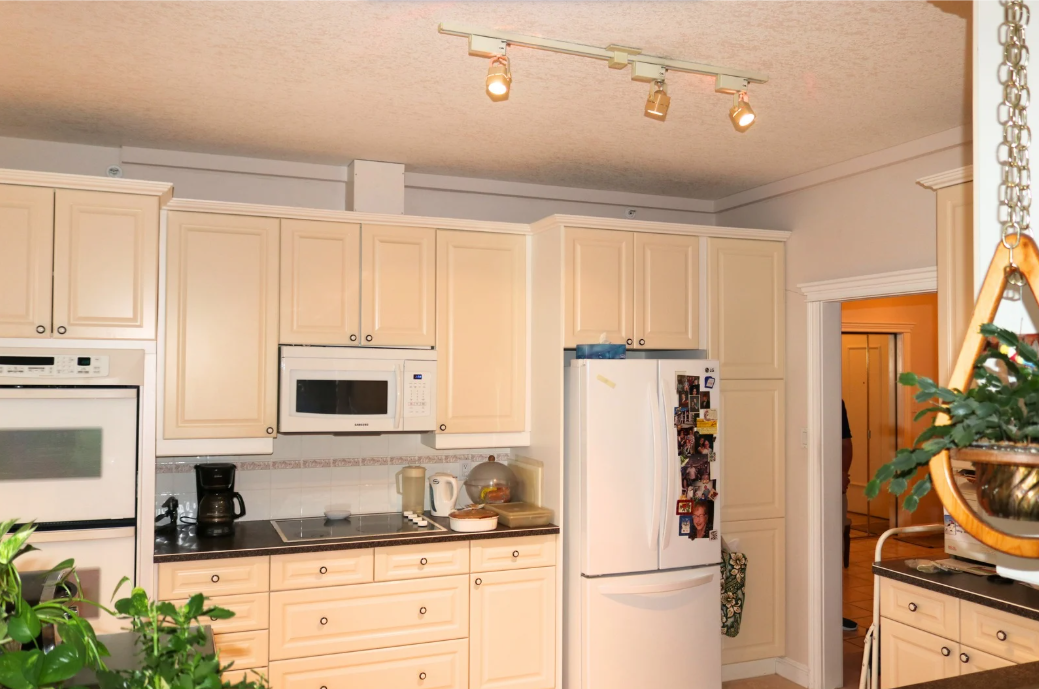 plumbing track installed and painted View of a kitchen with beige cabinets, black countertops, a white refrigerator covered with photos, a microwave,