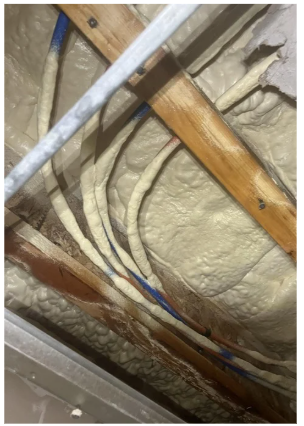 View of electrical wiring and Kitec plumbing pipes inside a wall with insulation.