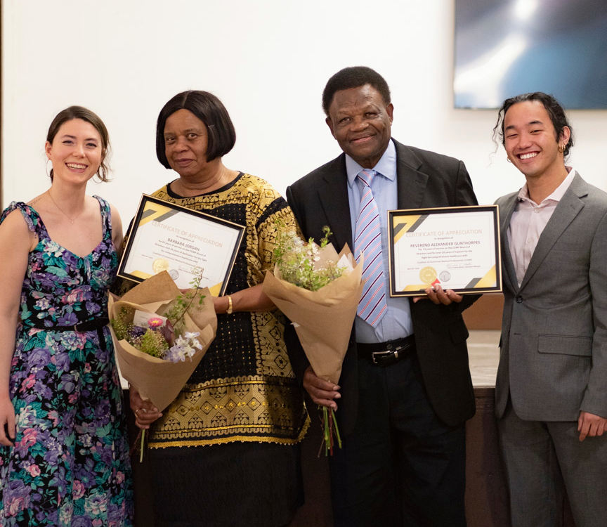 A group of four event attendees, with two holding awards and bouquets of flowers.