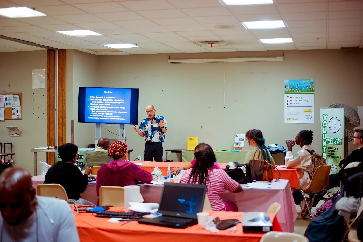 A volunteer doctor presents information to a large group on a healthcare topic of interest to the group.