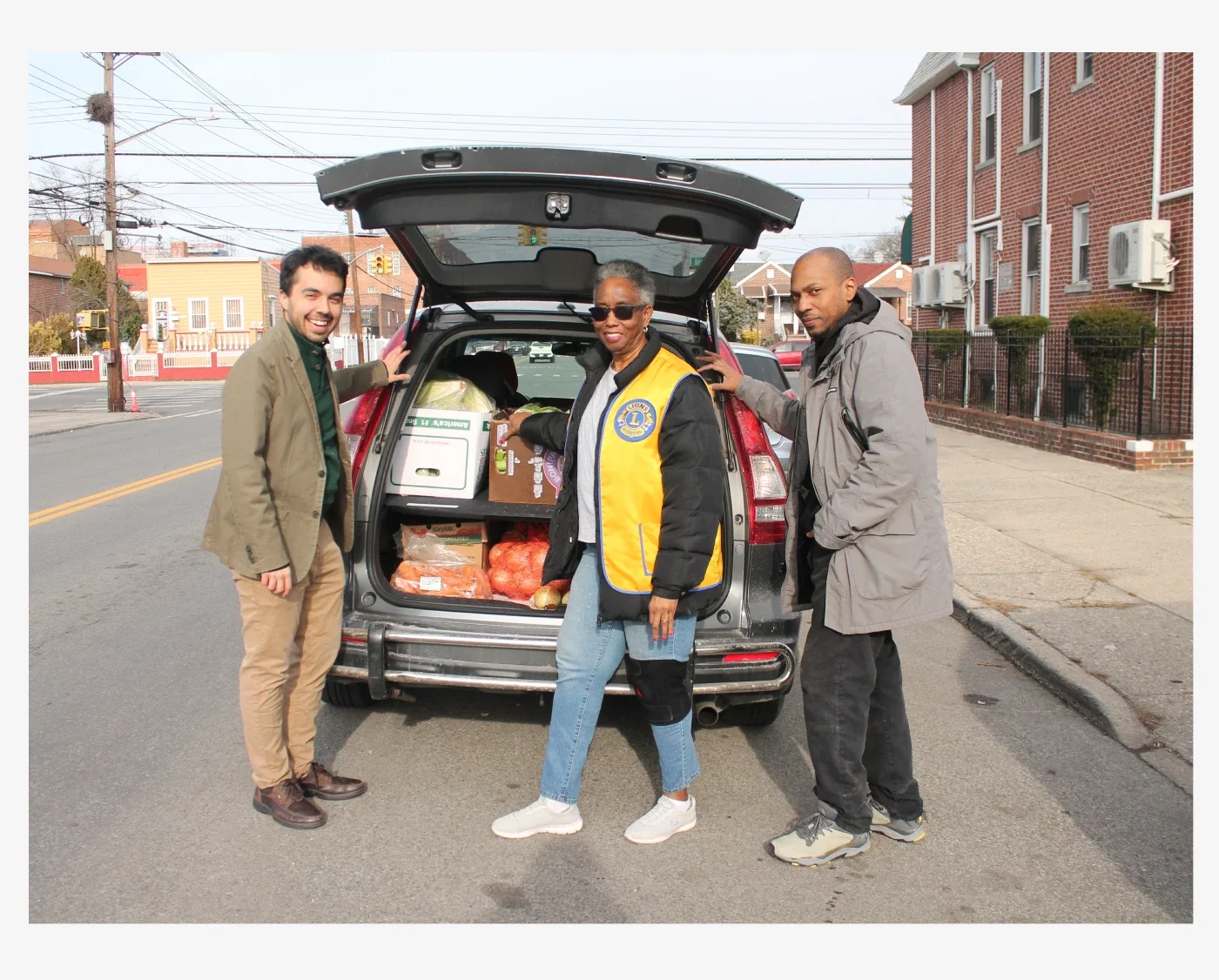 Three volunteers posing in front of a trunk of an SUV filled with donated fresh produce.