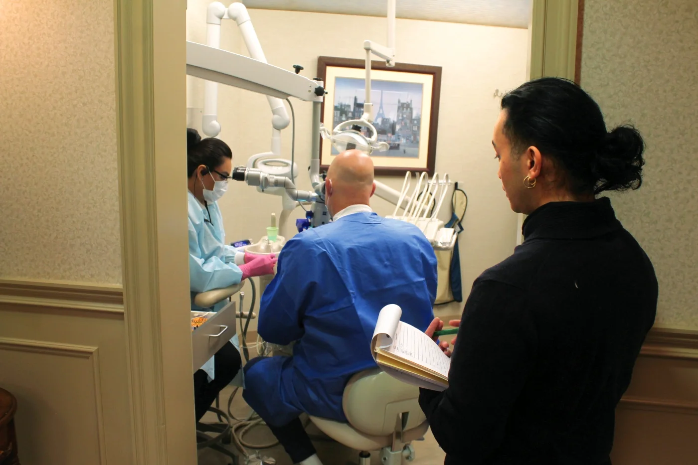 A volunteer dentist and his assistant perform a dental procedure while a volunteer advocates takes notes.