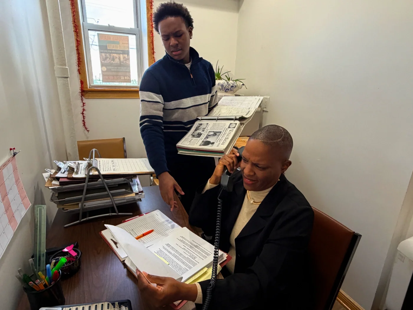 A volunteer does advocacy on the phone while another volunteer stands to her side and assists.