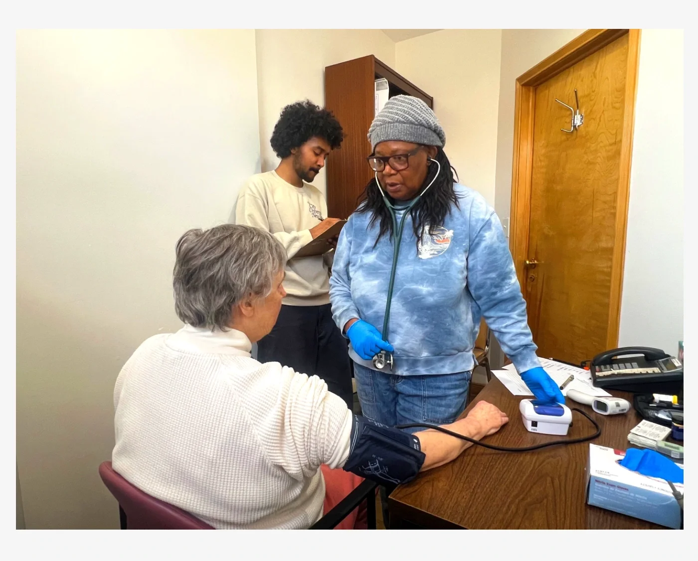 A volunteer nurse checking someone's blood pressure while an advocate takes notes.