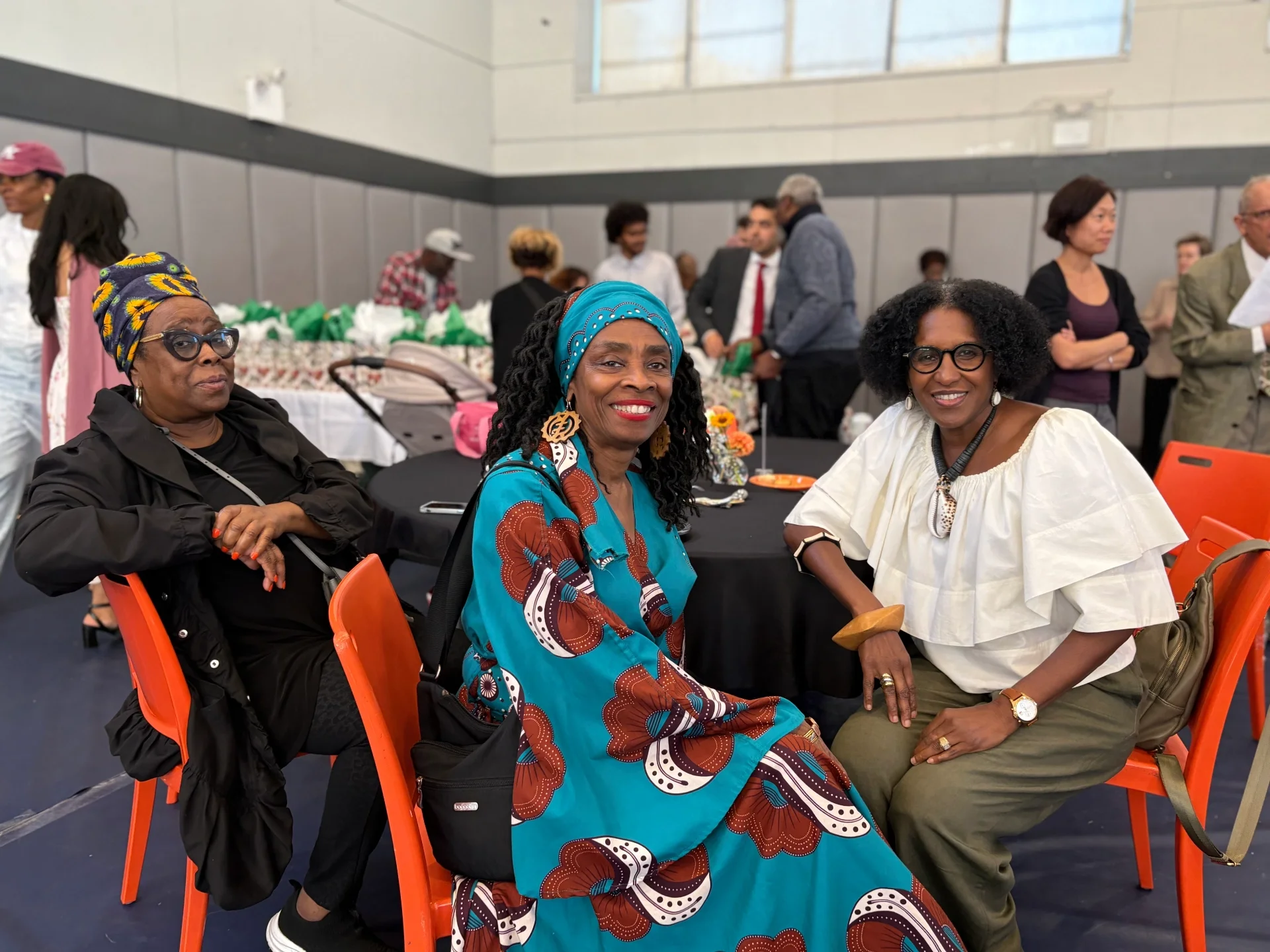 Three party attendees smile while sitting at a table with a black table cloth and orange chairs.
