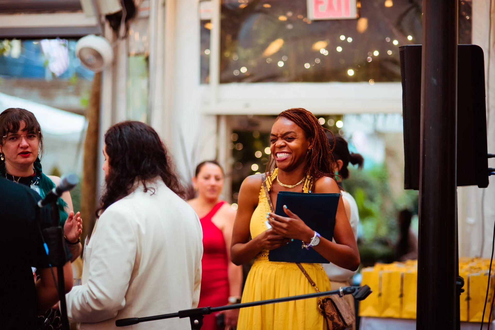 A volunteer in a yellow party dress smiles holding a black clipboard.