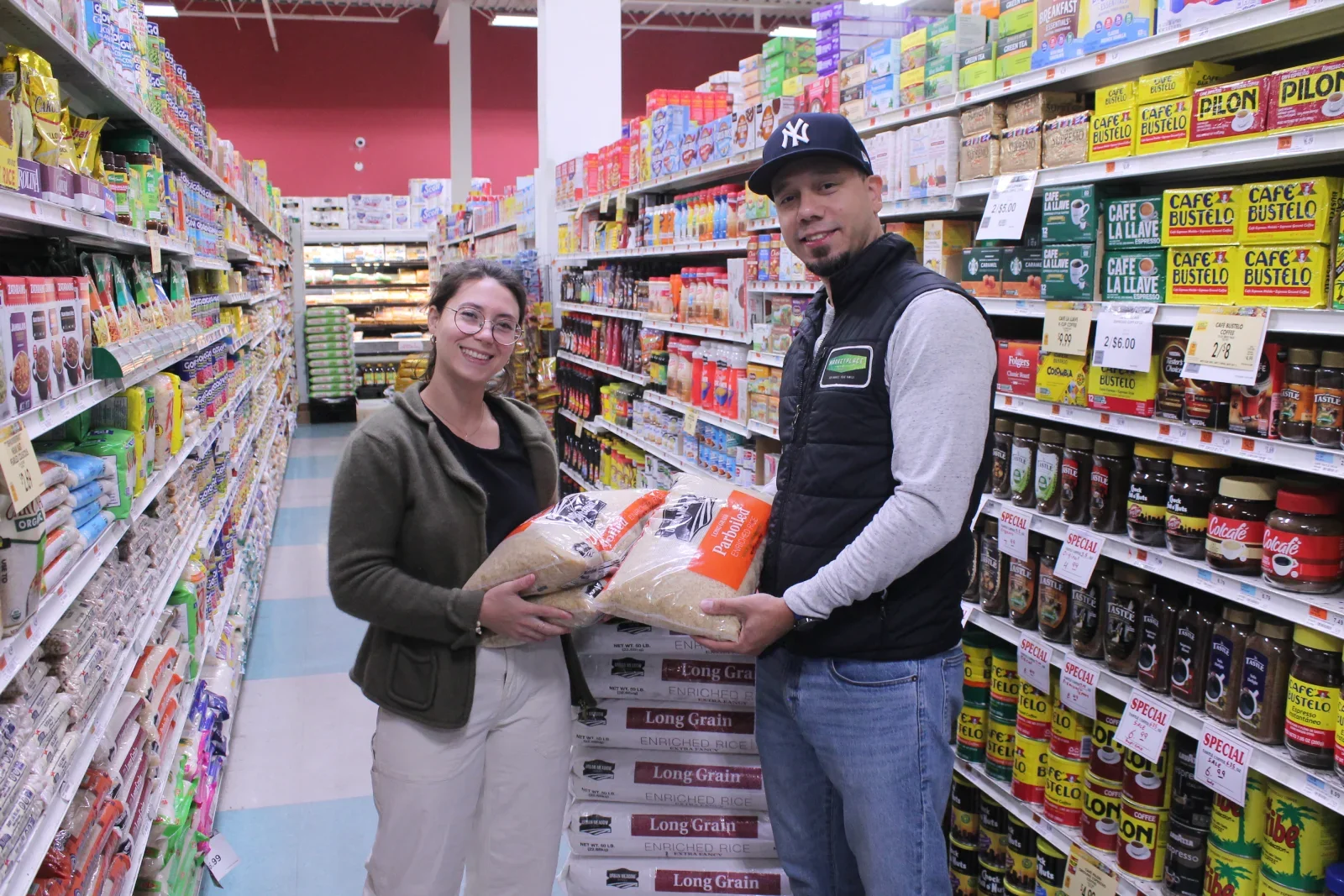 A CCMP volunteer at a grocery store holding a bag of rice with the owner of the store.