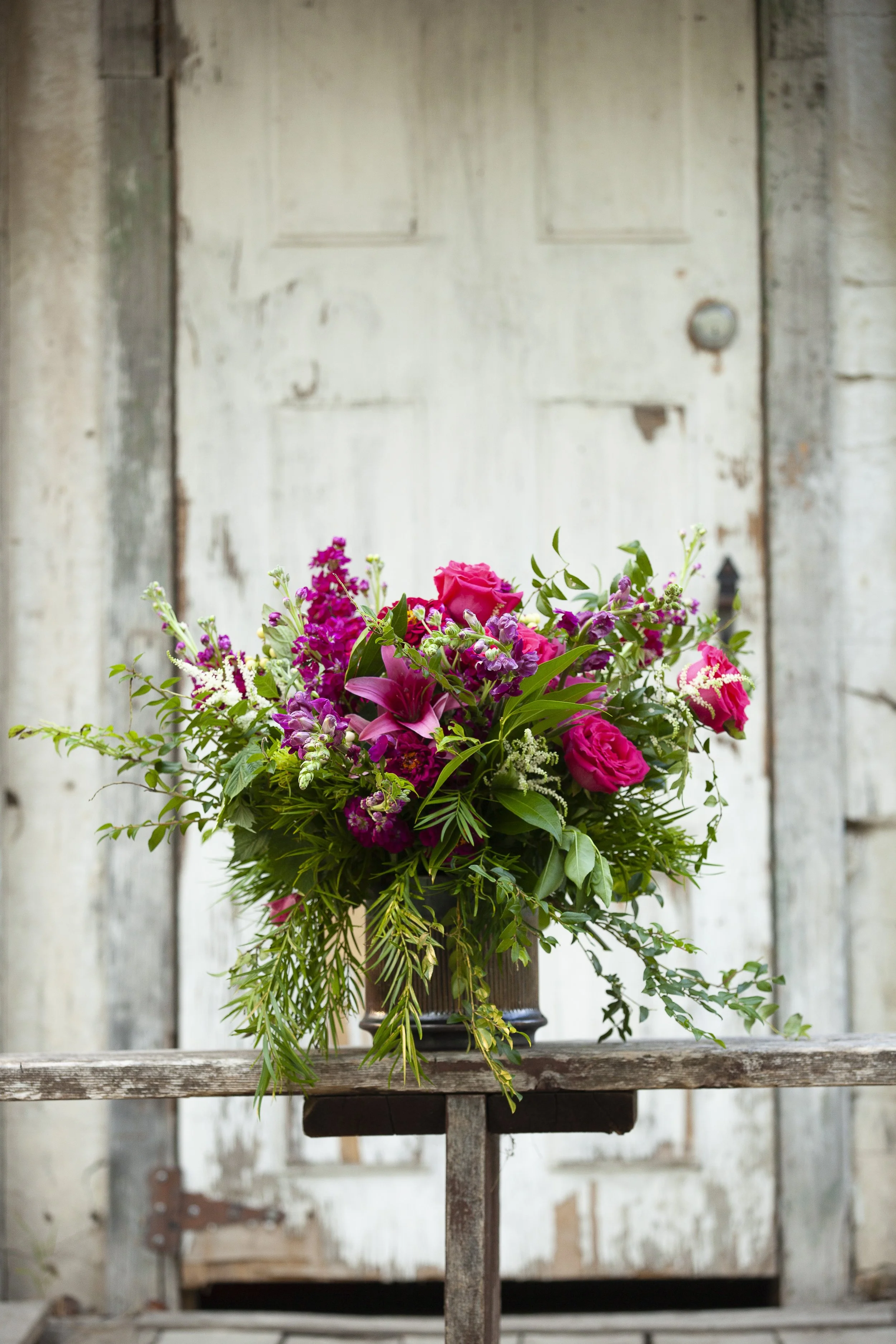 A colorful bouquet of pink and purple flowers on a rustic wooden table with a weathered white door in the background.
