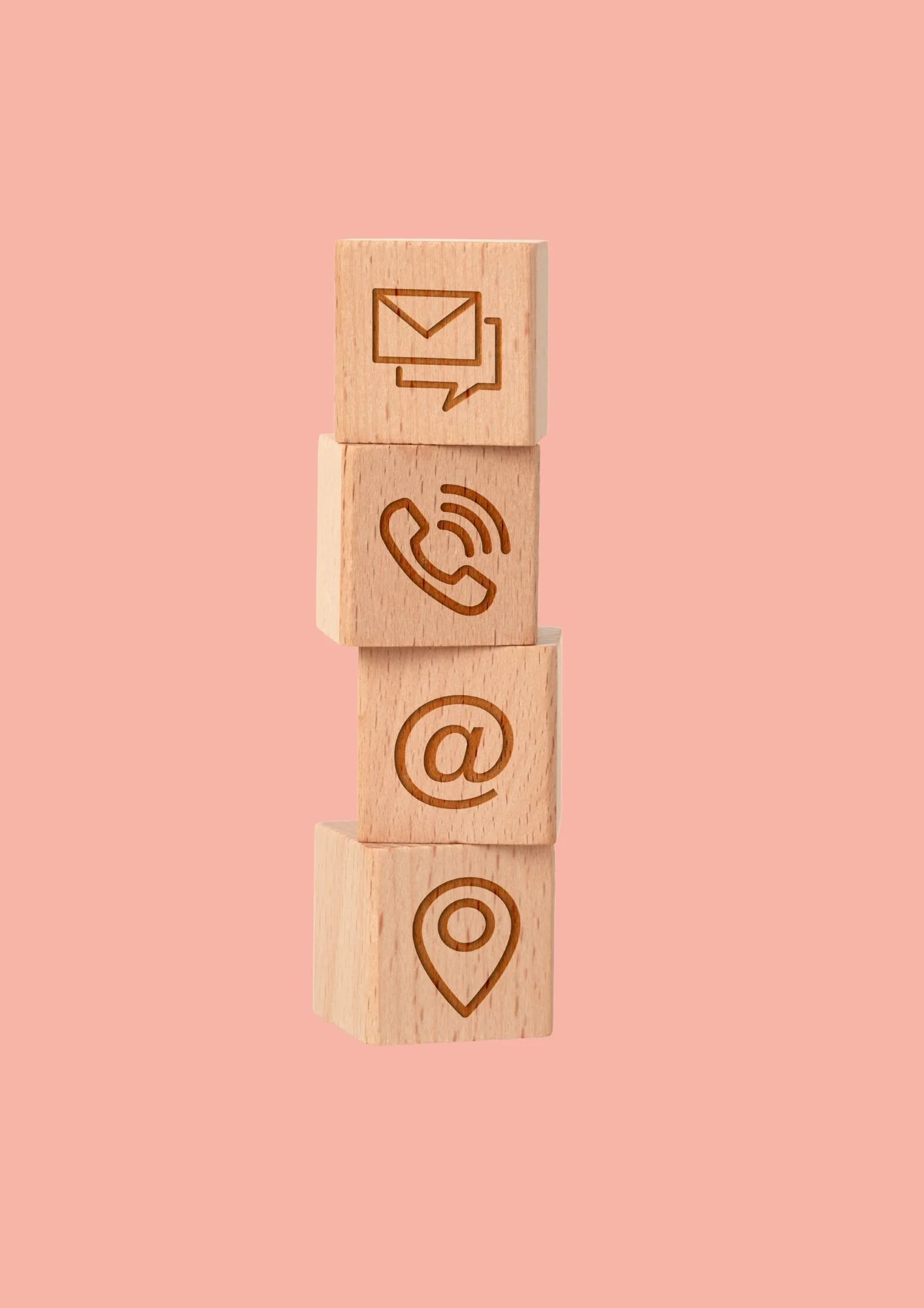 Stacked wooden cubes with social media icons: email, phone, email at symbol, and location pin on a pink background.