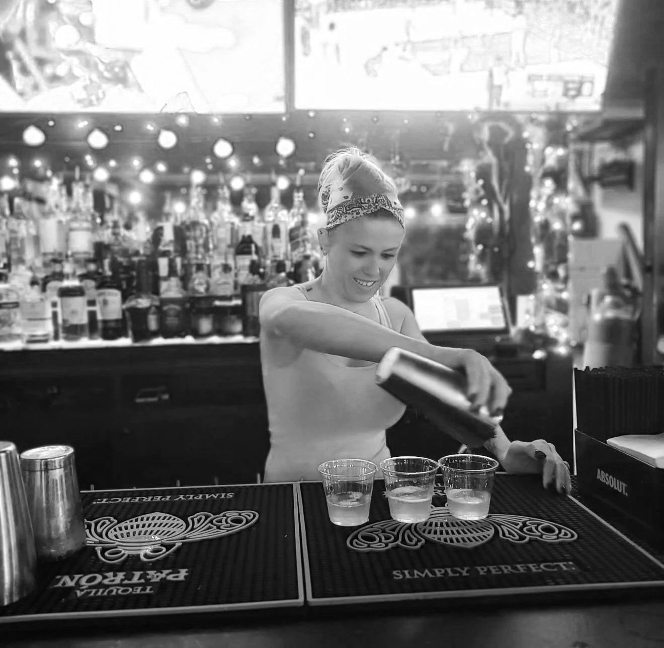 A woman working as a bartender at a bar, pouring a drink into glasses on the counter.