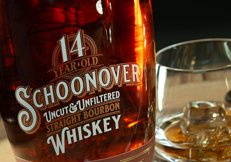 A bottle of 14-year-old Schoonover straight bourbon whiskey and a glass with ice cubes and whiskey.