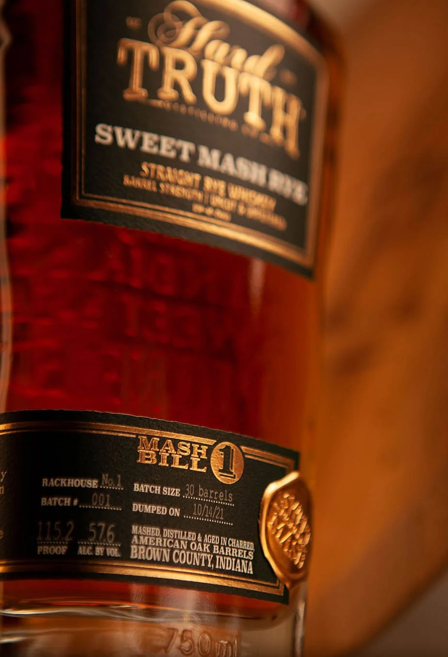 Close-up of a whiskey bottle with labels indicating it is a batch of American oak barrel-aged whiskey from Brown County, Indiana, with batch number 001 and proof 115.2.