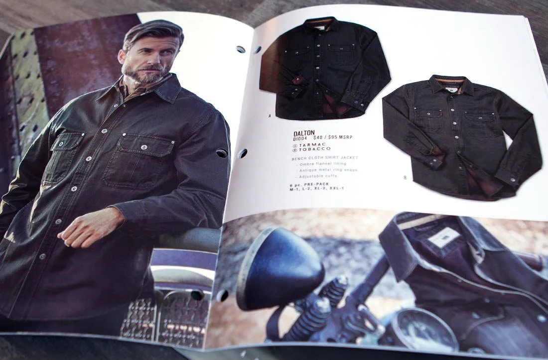 Open magazine featuring a man in a black denim shirt on the left page; on the right page, two black denim shirts, with one folded and the other laid flat. Below, part of a motorcycle's handlebar and seat are visible.