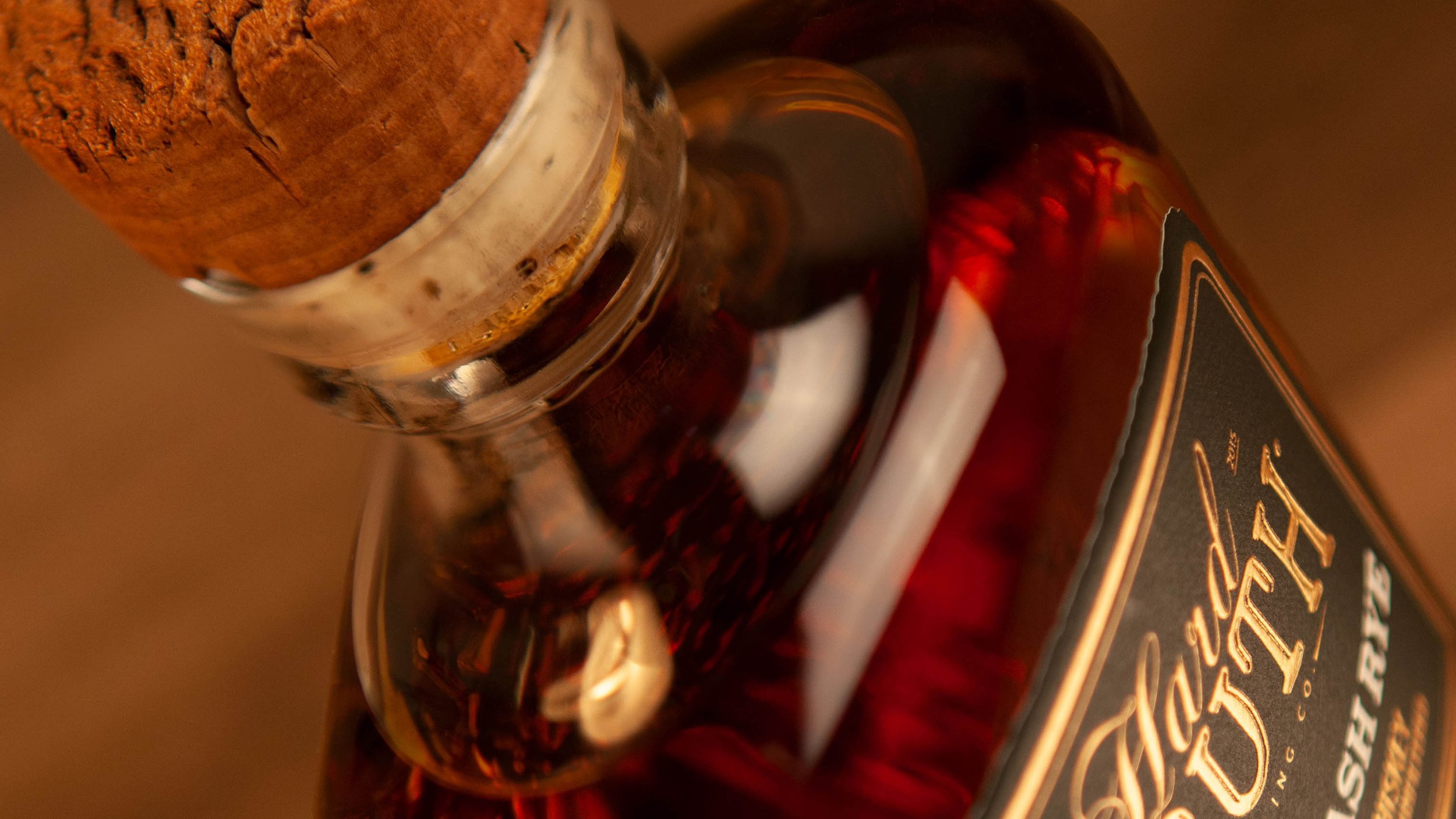 Close-up of a whiskey bottle with a cork stopper and a partially visible label, shot from an angle with warm, amber lighting.