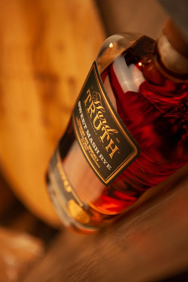 Close-up of a bottle of Angel's Envy bourbon whiskey placed on a wooden surface.