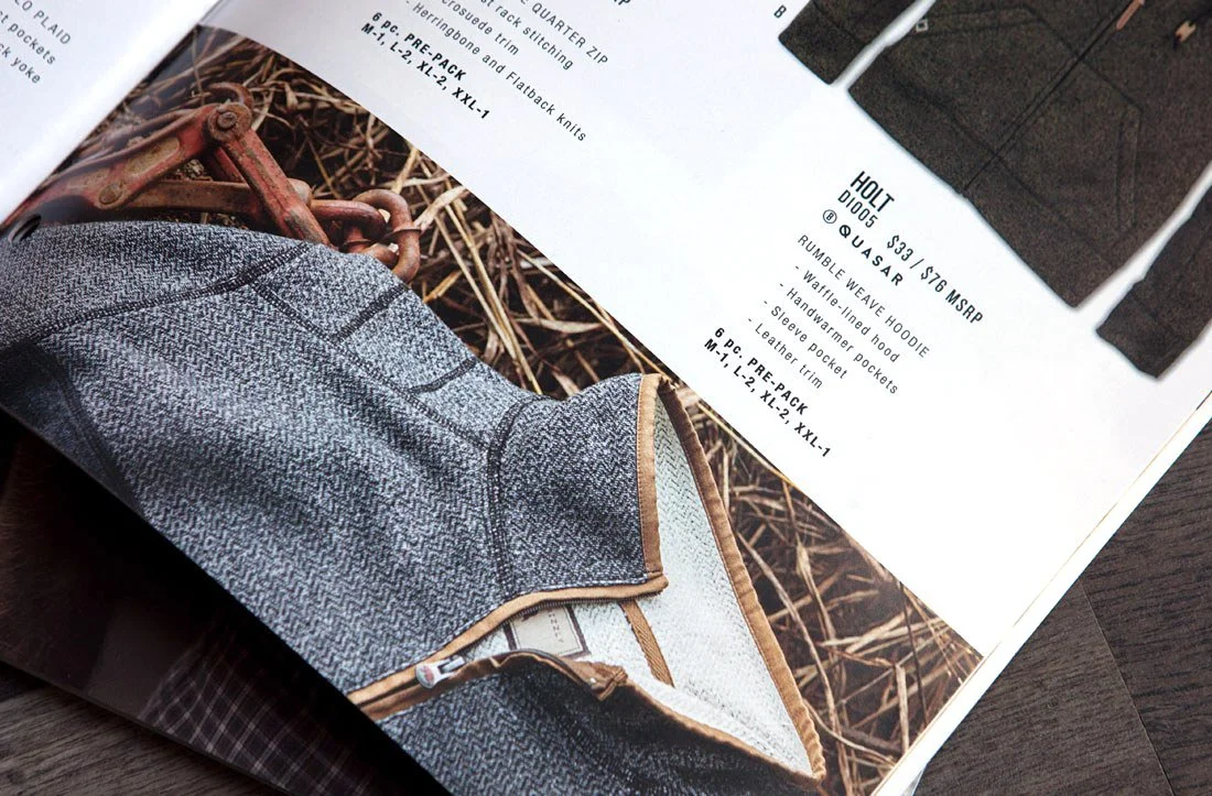 Page from a catalog showing a quilted gray hoodie with tan trim and a close-up of a rusty chain link fence on the opposite page.