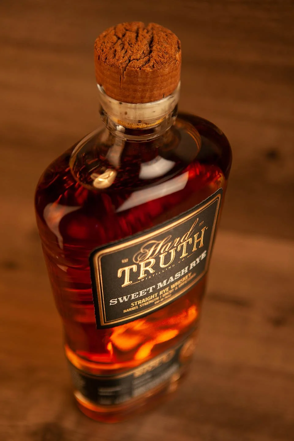 A bottle of whiskey with a cork stopper, labeled 'Hand 'TRUTH', 'Sweet Mash', and 'Straight Rye Whiskey' on a wooden surface.