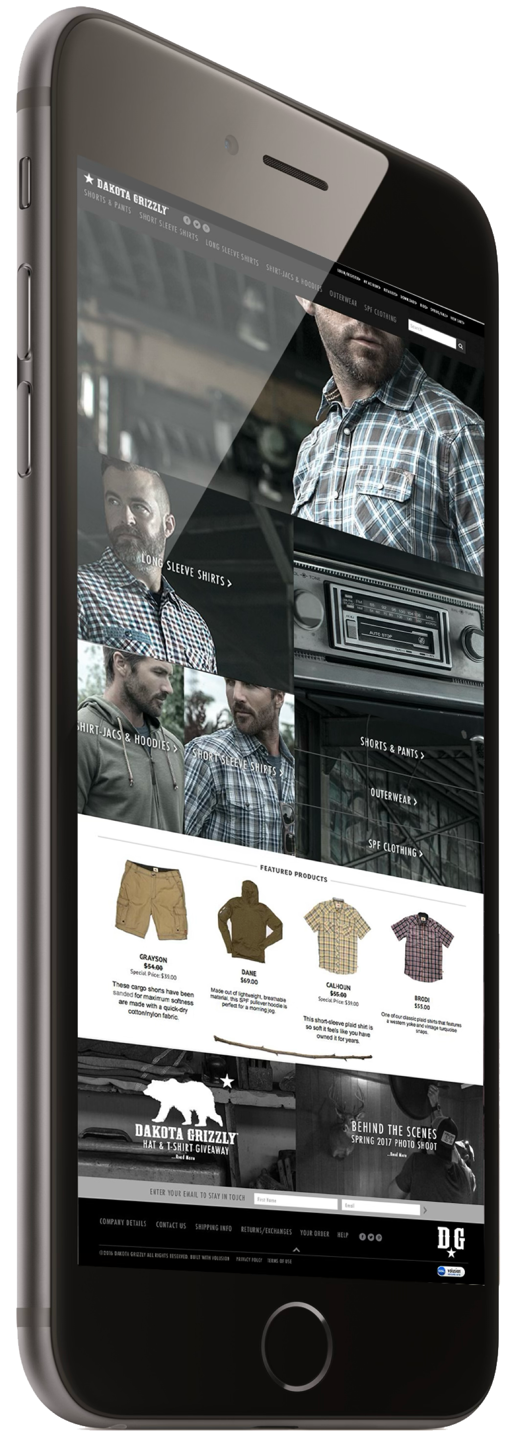 A smartphone displaying an online clothing store website for Dakota Grizzly, featuring plaid shirts, shorts, hoodies, outerwear, and accessories with models wearing the clothing.