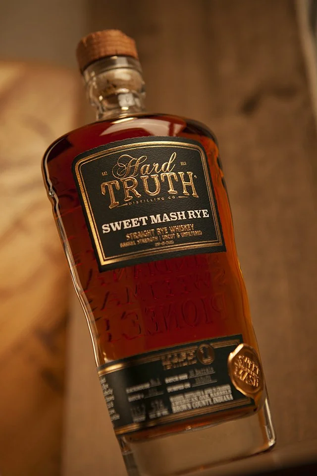A bottle of Hard Truth Sweet Mash Rye whiskey with a black and gold label.