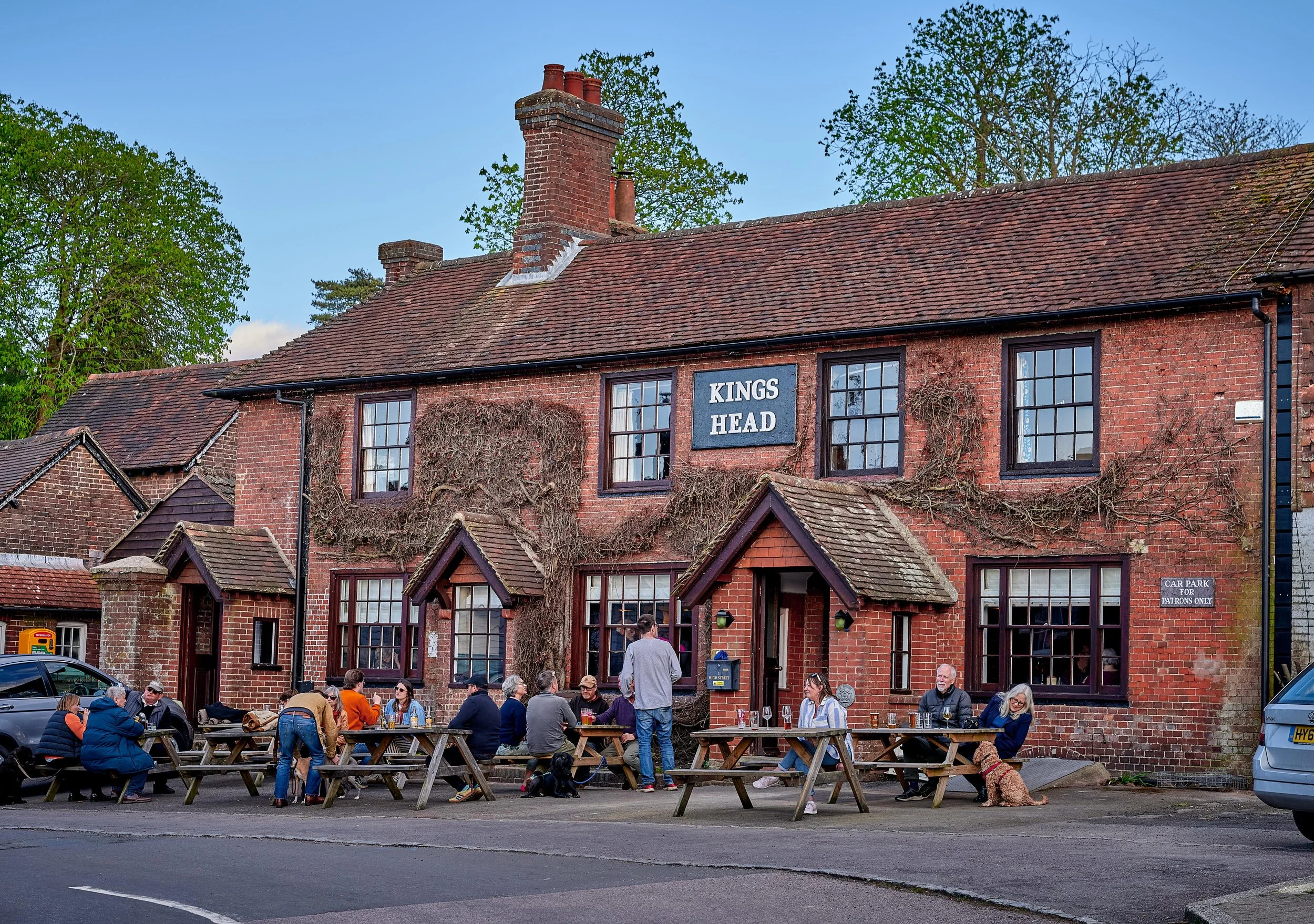 People sitting at picnic tables outside a brick pub called Kings Head with a sign and ivy on the building