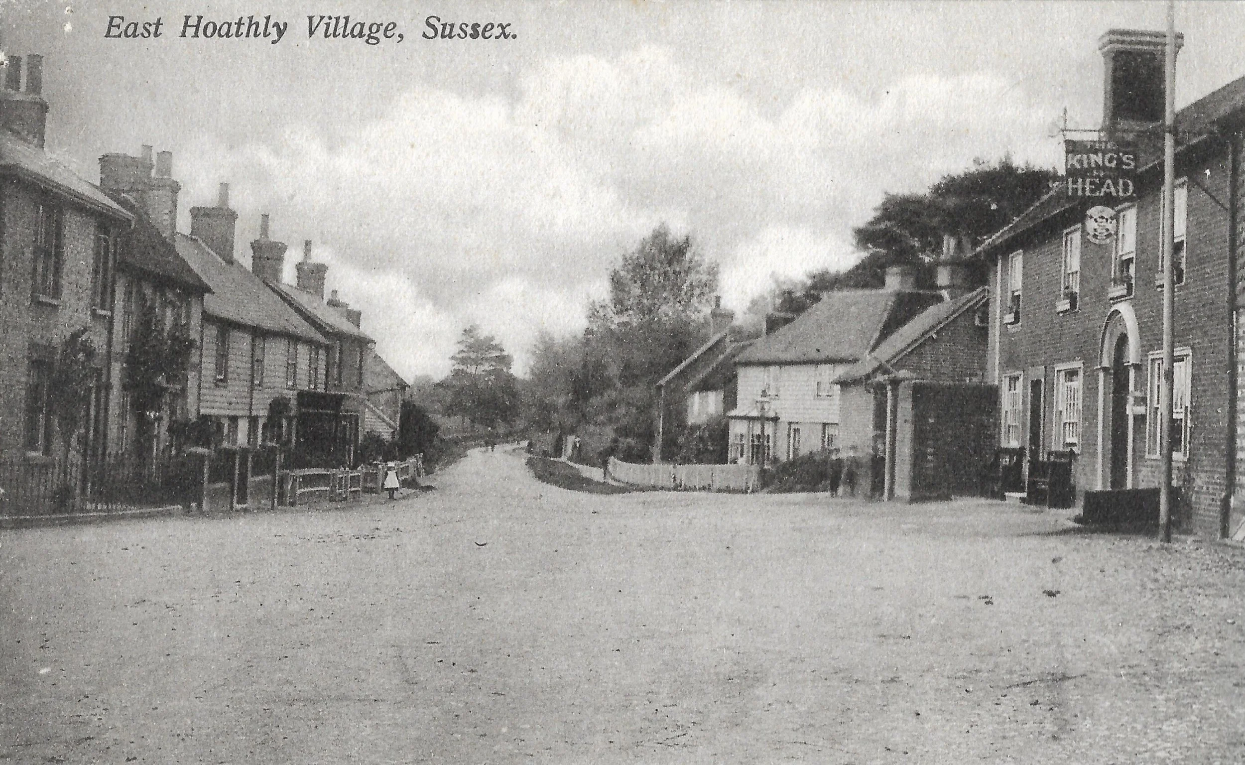 Black and white photograph of a rural village street with houses on either side, labeled East Hothing Village, Sussex, with a sign for The King's Head pub on the right.