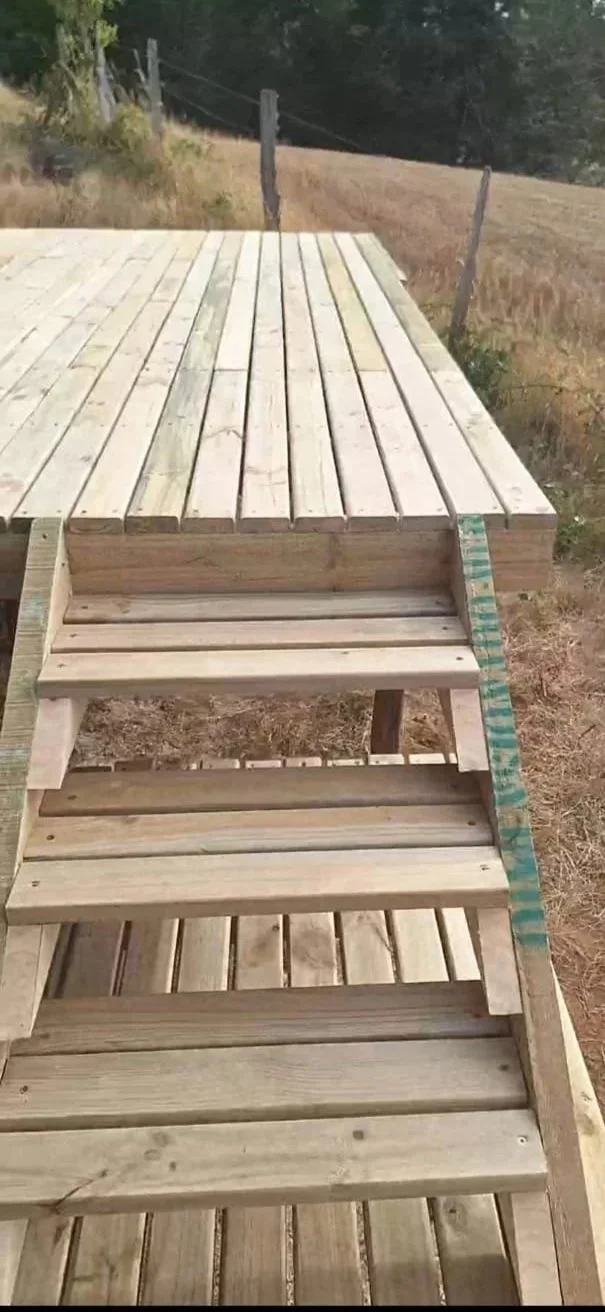 Escalera estructurada en madera en construcción, con pasos y tablas de madera en un entorno al aire libre.