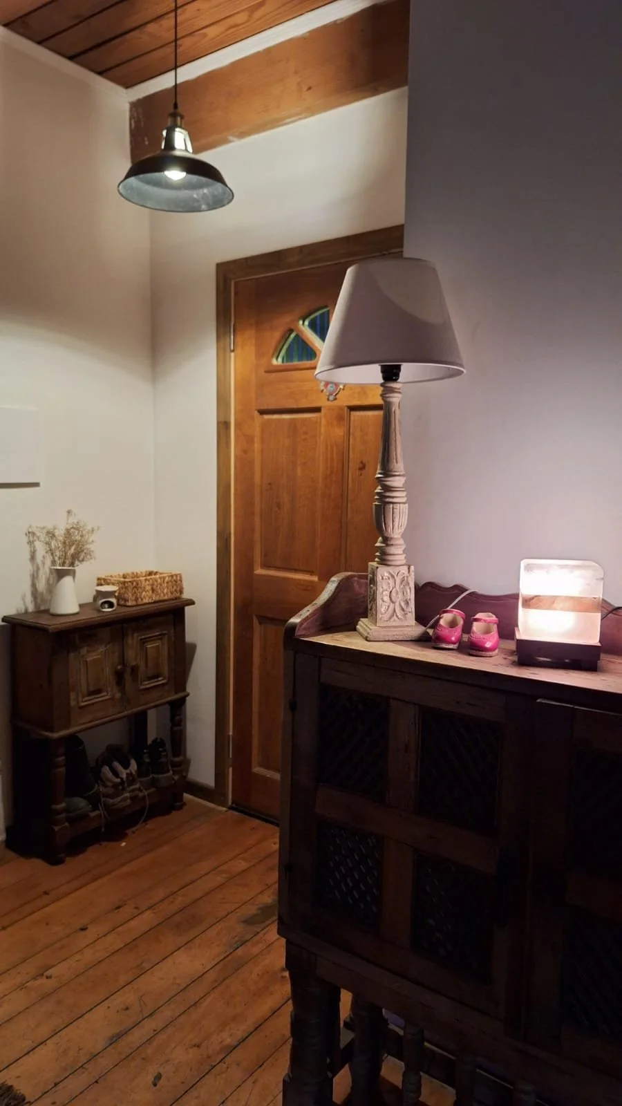 Entrada de una casa con puerta de madera, mesa con lámpara, decoración de zapatos rojos, y decoración de estilo rústico.