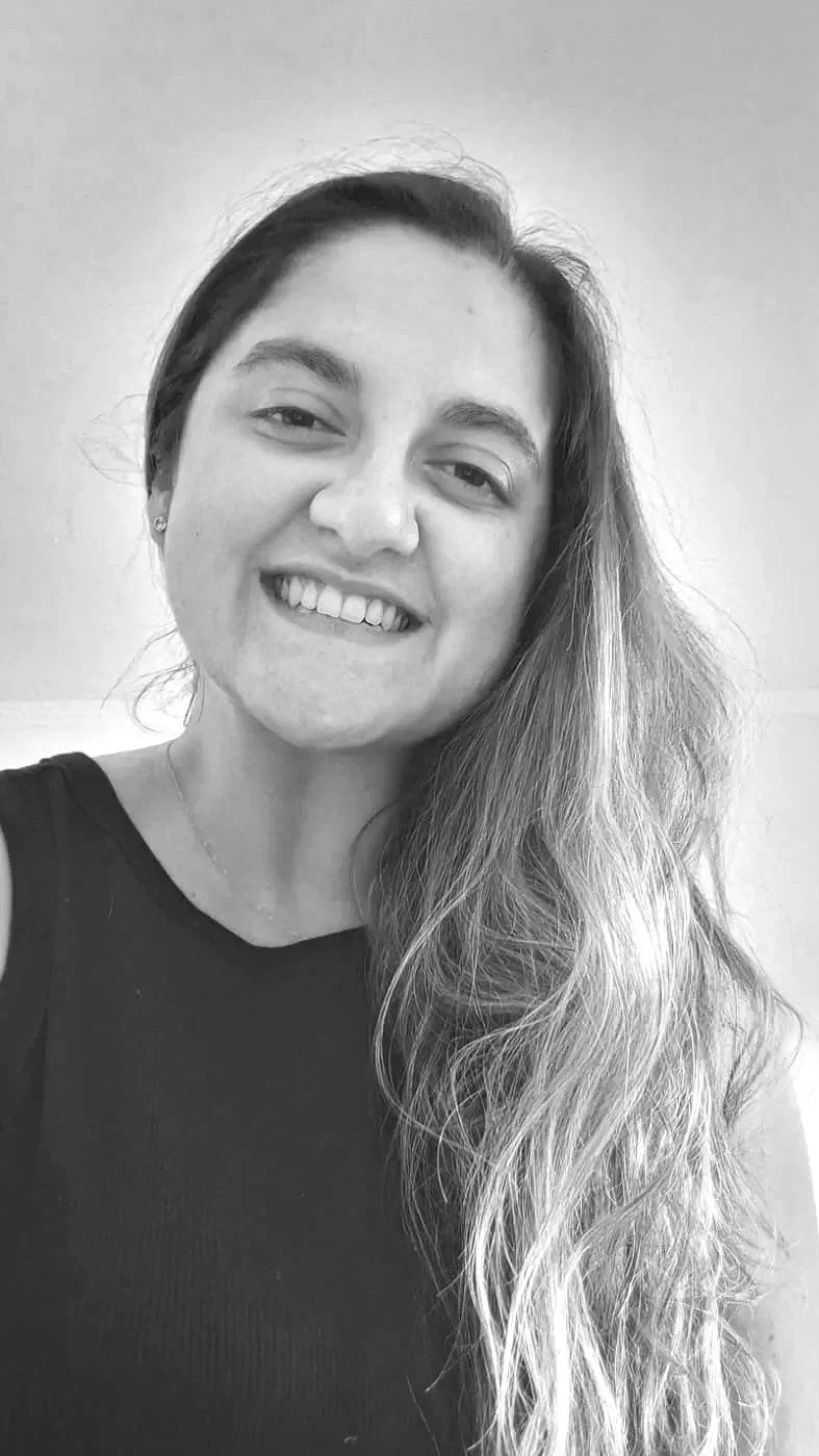 Retrato en blanco y negro de una mujer sonriendo, con cabello largo y ondulado, usando un top sin mangas y un collar.