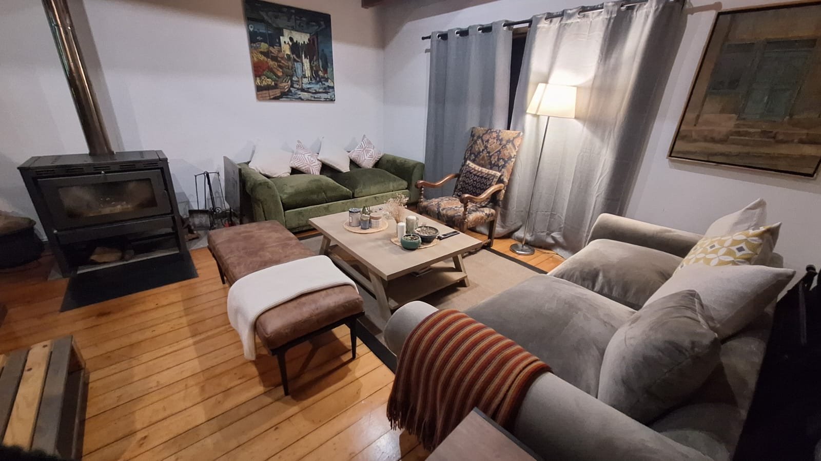 Sala de estar con sillones y una chimenea eléctrica, mesa de centro decorada, cuadros en las paredes y cortinas, en un ambiente acogedor.