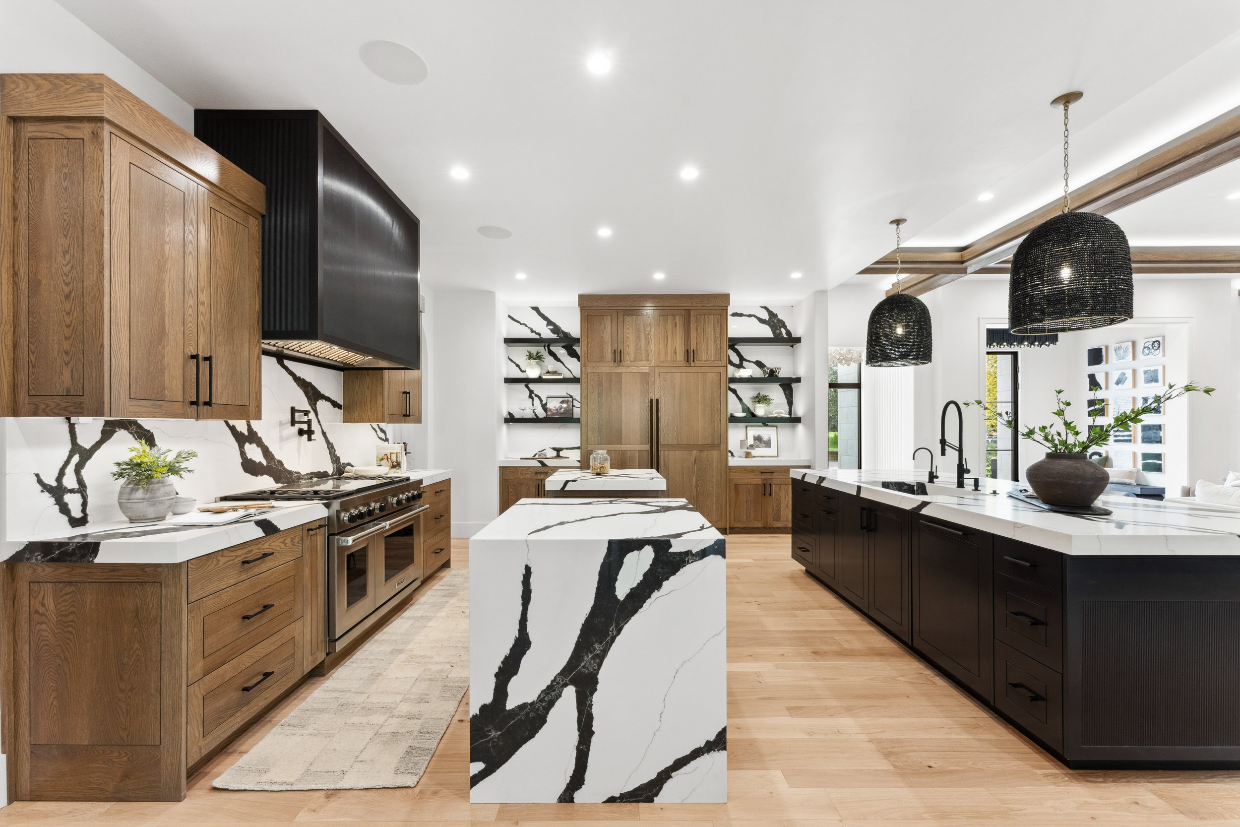 Contemporary kitchen featuring wooden and black cabinetry, a marble island and backsplash with black veining, black pendant lights, and open shelving with decorations.