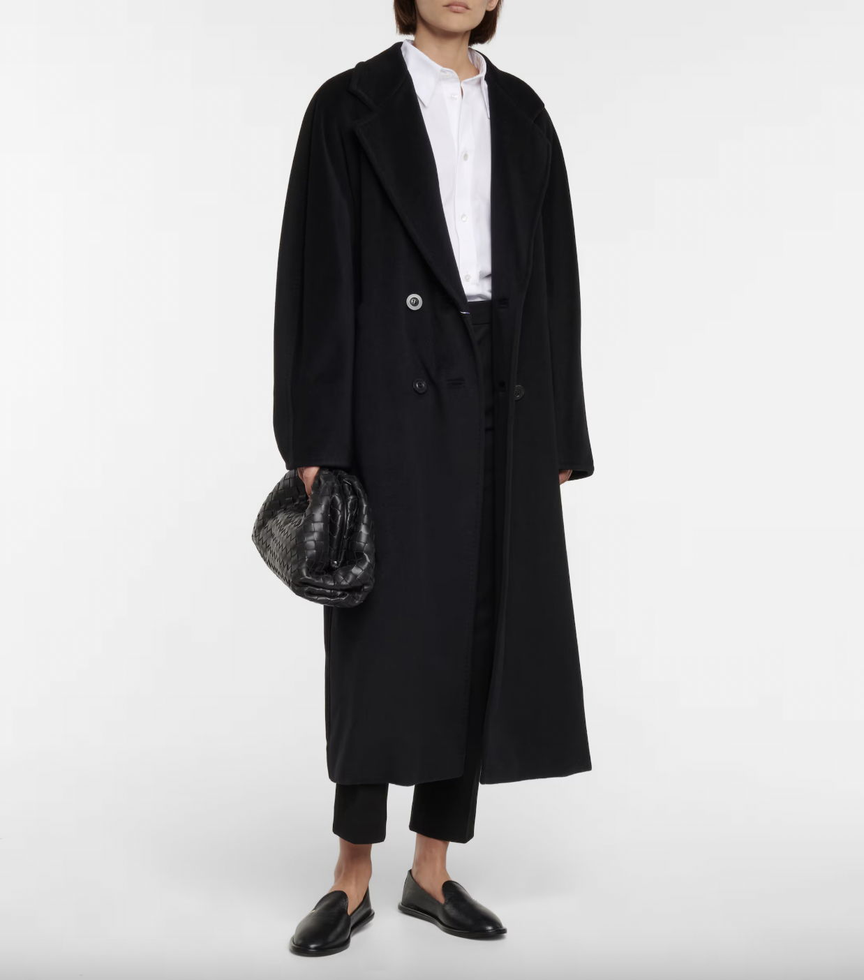 A woman in a black Max Mara Madame Wool and Cashmere coat, black cropped trousers, white cotton poplin shirt, and leather loafers, while holding a small Bottega Venetta bag