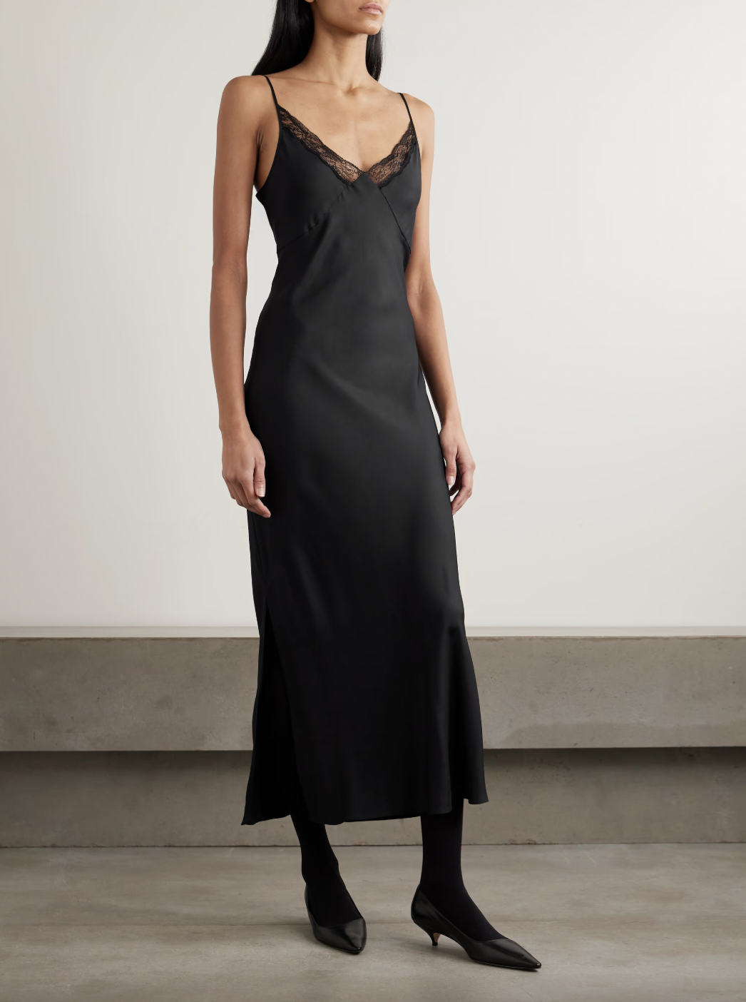 A woman wearing THE ROW Barina lace-trimmed silk-twill midi dress in black with black opaque tights and black pointy kitten heel pumps