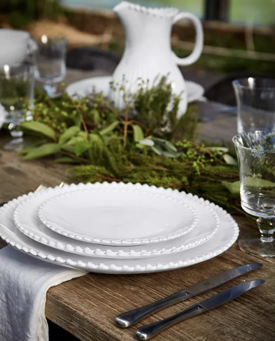 Costa Nova White Pearl Dinner Plate on a rustic wood banquet table with a linen napkin and green leaf centerpiece