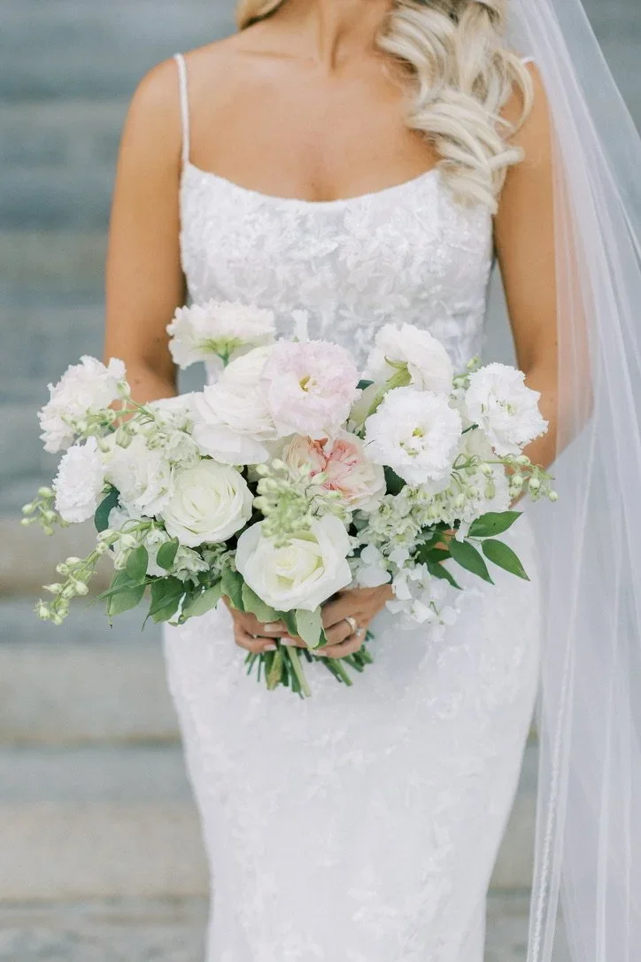 Bride in a white lace wedding dress holding a bouquet of white and pale pink flowers.