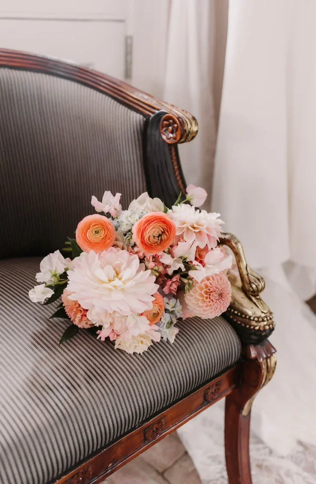 A bouquet of pink and white flowers resting on a vintage-style upholstered sofa with dark wood and ornate detailing.