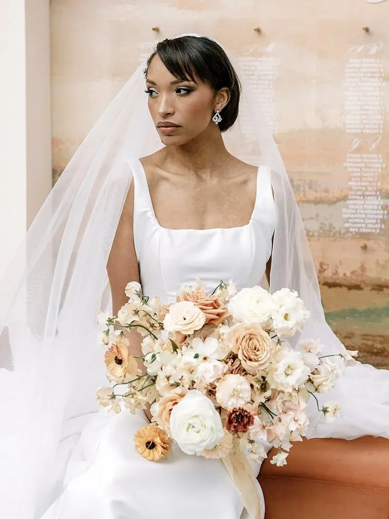 A woman in a white wedding dress holding a bouquet of pastel-colored flowers.
