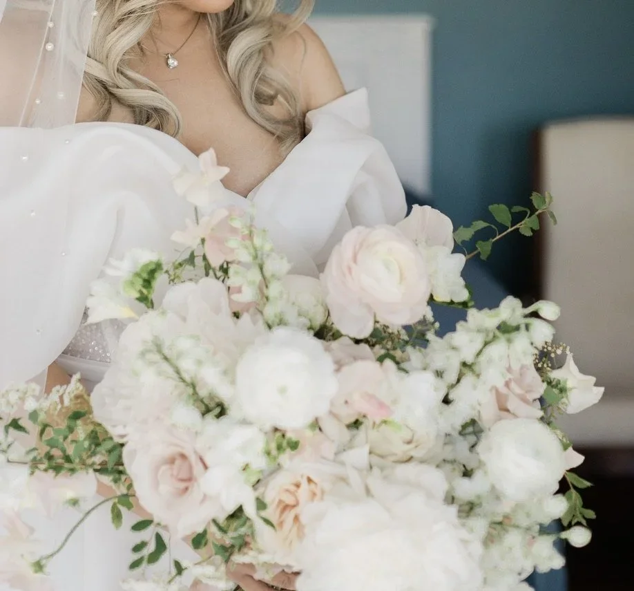 A bride holding a large bouquet of white and soft pink flowers, with her blonde hair and part of her white wedding dress visible.