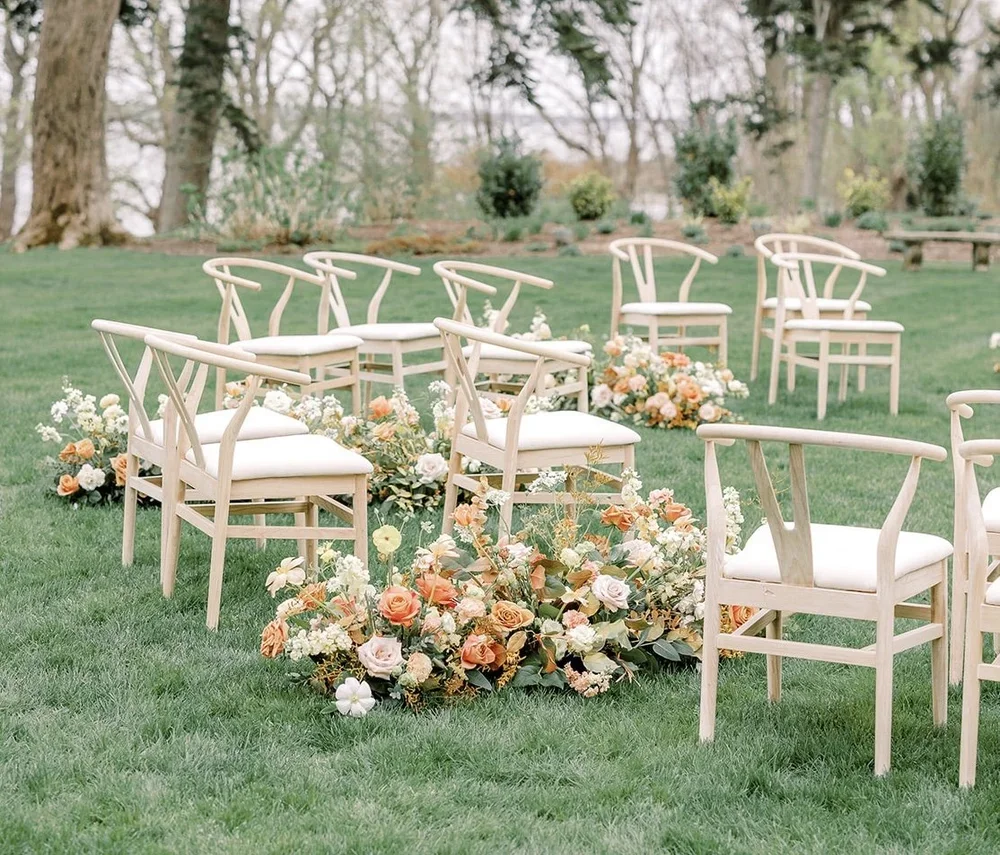 Chairs arranged outdoors for a wedding ceremony with floral decorations on a grassy area.