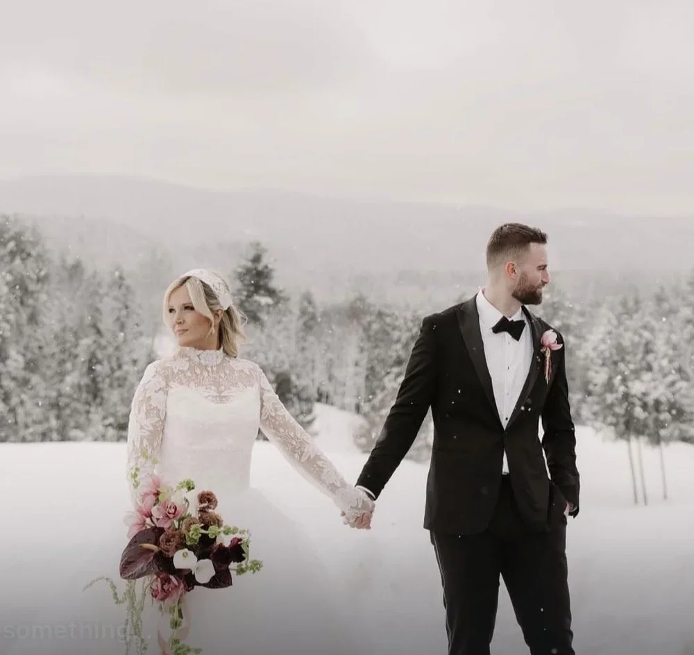 A bride and groom holding hands outdoors in a snowy landscape, with the bride holding a bouquet of flowers.